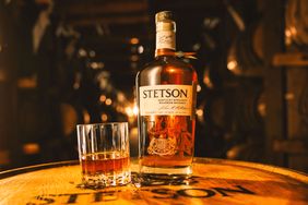 Bottle of Stetson bourbon and a glass of whiskey on a wooden barrel in a dimly lit barrel room