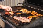 Grilling various meats on a barbecue grill hand holding tongs turning food