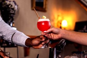 A bartender and a patron exchanging a cocktail in a glass with foam