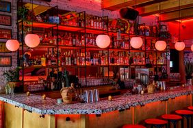 A stylish bar with modern decor, featuring shelves of bottles and globed pendant lights above the counter with stools
