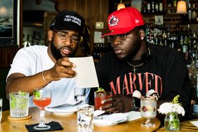 Tim Grant and Paul McGhie seated at a table in a restaurant examining a menu while drinks and plates are on the table