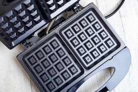 A waffle iron with its lid open showing the cooking plates with square patterns