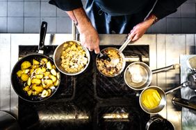Chef preparing dishes at a stove frying pan with potatoes and other cooking ingredients visible