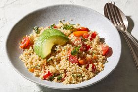A bowl of quinoa salad topped with avocado slices and cherry tomatoes served with fresh herbs