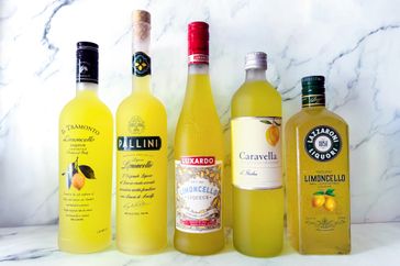 Five bottles of limoncello from different brands are arranged in a row on a marble background