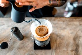 A hand pouring liquid into a coffee filter with coffee grounds on a wooden surface