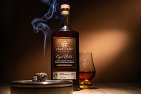 A bottle of Starlight Distillery Cigar Batch bourbon accompanied by a smoking cigar and a glass of whiskey