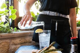 A server pours a bottle of sparkling water into a glass for a customer.