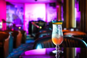 A cocktail on a table in a dimly lit lounge with vibrant lighting in the background