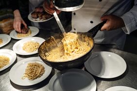 Chef serving pasta onto plates in a kitchen