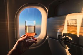 A hand holding a glass of wine near an airplane window during a flight